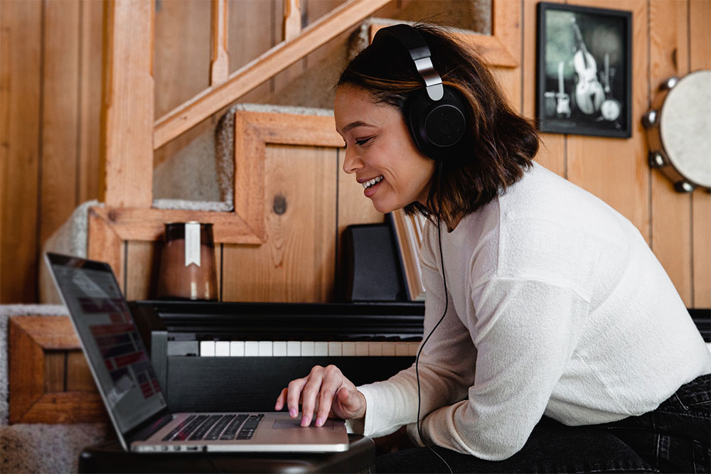 Young woman in front of laptop with headphones on smiling at the screen